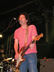 Kaplan playing guitar onstage and singing into a microphone