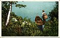 A postcard showing a man carrying a pack basket, standing on a lakeshore beside a guideboat.