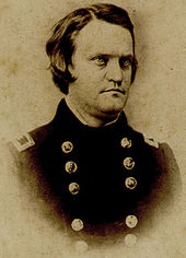 A dark haired, clean-shaven man dressed in a double-breasted military uniform
