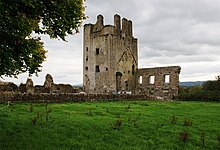 A photo of a ruined, square, thick-walled tower and an adjacent house of which only one wall with big windows remains