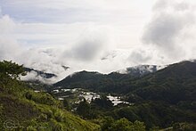 Des rizières en terrasse avec de petits bâtiments dans un paysage de montagnes très vertes.