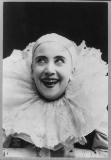 Pilar Morin as clown/mime, in white baldcap and a large white collar: head and shoulders, facing slightly left; smiling