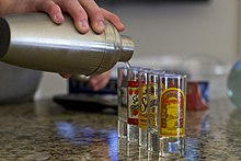 Image of liquor being poured into multiple shot glasses