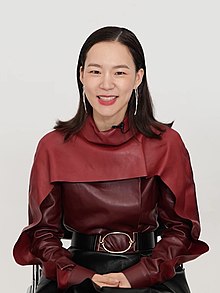Han wearing a red top and smiling against a white background.