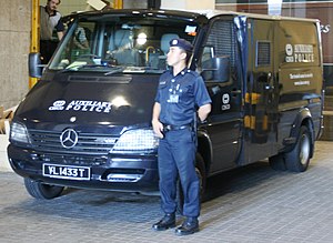 A Certis CISCO auxiliary police officer stands guard beside an armoured truck while his colleagues deliver high-valued goods to and from commercial clients at Change Alley, Singapore. CISCO Security.jpg