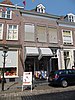 Huis met schilddak en fraaie Empire lijstgevel met grote vensters waarin ramen met witte roedenverdeling (beneden ten dele verwijderd) en witte deuromlijsting met gecanneleerde pilasters, kroonlijst, en gesneden bovenlicht