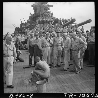 The crewmen of the battleship USS New Jersey watch a Japanese prisoner of war bathe himself before he is issued GI clothing. [Nov 1944][14]