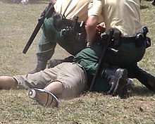 German policemen subdue an offender. Both officers have nightsticks, sidearms, handcuffs and radios clipped onto their duty belts. BayBePoFestnahme.jpg