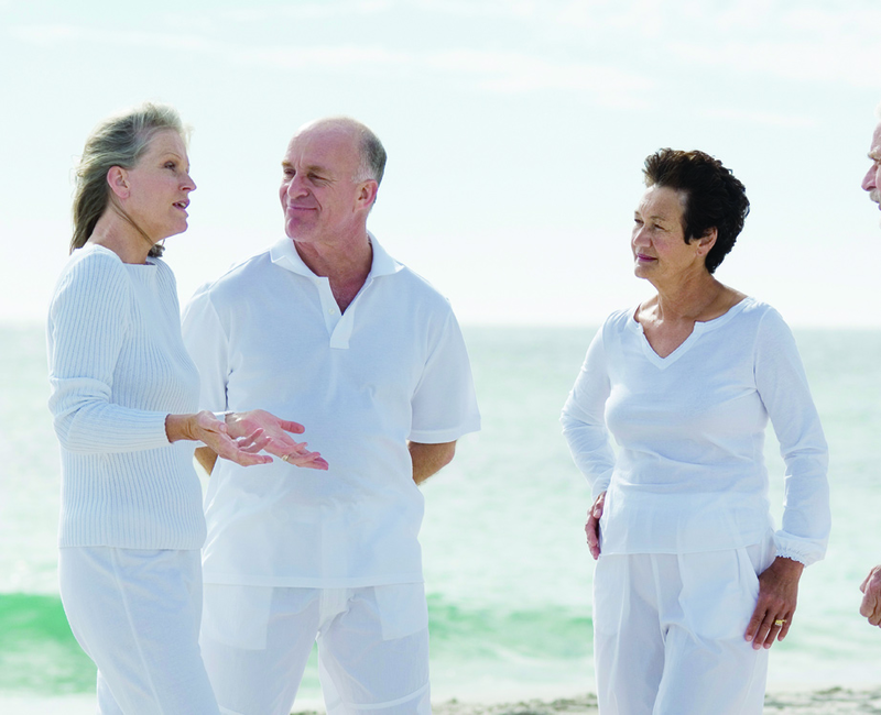 Three eldery people stand on a beach, in conversation.