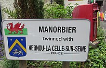 Photo d'un panneau blanc portant une inscription en anglais illustrée avec le drapeau gallois et le blason de Vernou-la-Celle-sur-Seine