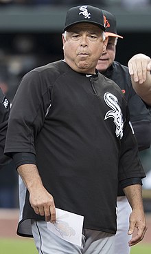 An man in a black baseball jersey, gray pants, and a black cap