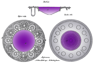 A large circular glass lens with a flat top and a stepped domed bottom. The glass is purple, with the shade darkening towards the top. The glass is set in a wide and ornate circular frame engraved with a semi-geometric ring-of-roundels design that looks a bit Art Deco, although from 1834.