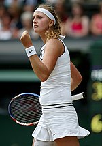 A blond-haired woman wearing a white attire, celebrating after winning a point