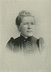 B&W portrait photo of a blonde woman with her hair in an up-do, wearing a dark blouse.