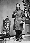 Photo of a dark-haired, bearded man with his right hand thrust into his coat like Napoleon. He wears a dark military uniform with two rows of buttons.