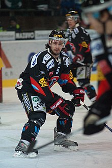 Photographie couleur d’un hockeyeur en plein match, en train de patiner vers l’arrière, entre deux coéquipiers plus flou à l’avant et à l’arrière-plan