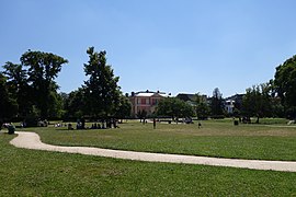 Vaste pelouse ensoleillée, avec quelques arbres, la Folie est au fond au milieu.