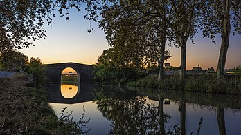 Ponte de Caylus refletida no Canal do Midi em Villeneuve-lès-Béziers, França. O canal artificial de navegação francês do Midi conecta dois vales fluviais separados e liga Toulouse ao mar Mediterrâneo desde o século XVII. Inicialmente era chamado “Canal Real de Languedoc”, os revolucionários o renomearam como “Canal do Midi” em 1789. A partir do século XIX, o canal lateral do Garona, estendeu o canal do Midi para fornecer uma via navegável do Oceano Atlântico para o Mar Mediterrâneo: a combinação dos dois canais é chamada “Canal dos Dois Mares”. Muito utilizado para o transporte de mercadorias, o canal do Midi está agora convertido em turismo fluvial. Desde 1996, está inscrito na Lista do Patrimônio Mundial da UNESCO. (definição 7 207 × 4 054)