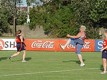 Three players in sports wear on a grassy field. One player has a foot in the air, as if they had just kicked a soccer ball.