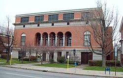 A three-story brick building on a stone foundation with a set of recessed arched openings in the center and a flat roof