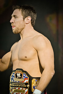 Le catcheur américain Bryan Danielson (alias Daniel Bryan), de profil. Il est torse nu et porte autour de la taille la ceinture de champion des États-Unis.