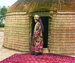 Woman in traditional dress standing on rug in front of yurt, 1911