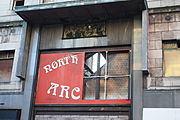 A large, damaged red shop sign, with white lettering, displaying "North-" and "Arc-". The right side is missing.