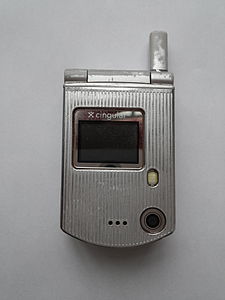 The front of a small, silver flip-phone, shut, taken against a white background.