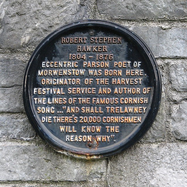 A black circular plaque with gold-coloured lettering. It reads: ROBERT STEPHEN HAWKER 1804 – 1875 ECCENTRIC PARSON POET OF MORWENSTOW WAS BORN HERE. ORIGINATOR OF THE HARVEST FESTIVAL SERVICE AND AUTHOR OF THE LINES OF THE FAMOUS CORNISH SONG ..."AND SHALL TRELAWNEY DIE THERE'S 20,000 CORNISHMEN WILL KNOW THE REASON WHY".
