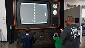 Two children are seen playing a game of Pong on a large-scale monitor.