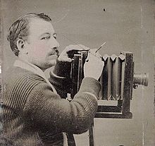 Dark-haired man with small moustache; operating large bellows camera