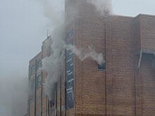 Upper portion of brick building with smoke pouring from windows