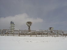 Three concrete radio towers with a fence between them and the camera