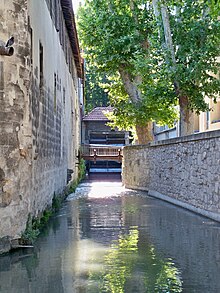 Vue sur le canal de Vaucluse, au niveau de l'eau, avec une roue à aubes en arrière-plan