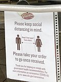 Sign reads "Please keep social distancing in mind. Keep 6 feet apart from one another. Please take your order to go once received. Thank you for helping us comply with govermental health recommedations."