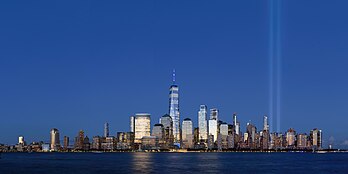 Tribute in Light (como visto em 2020) em memória dos atentados de 11 de setembro de 2001. O Tribute in Light é uma instalação artística consistindo em 88 holofotes verticais dispostos em duas colunas de luz para representar as Torres Gêmeas. Fica seis quarteirões ao sul do World Trade Center, no topo do Battery Parking Garage na cidade de Nova Iorque. O Tribute in Light começou como uma comemoração temporária dos ataques no início de 2002, mas tornou-se um evento anual, atualmente produzido em 11 de setembro pela Municipal Art Society de Nova Iorque. (definição 11 500 × 5 750)