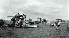 Photo noir et blanc de trois canons en batterie, sur des affûts surélevés, les servants s'affairant.