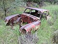 The remains of an old car near the little house.