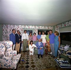 Семейный групповой портрет в солярии с занавесками в цветочек и обивкой, где все стоят за сидящим Джо, Джеки стоит на коленях рядом с ним