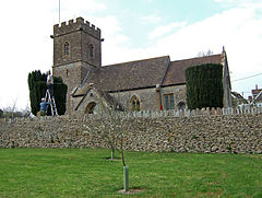Stone building with square tower behind stone wall.