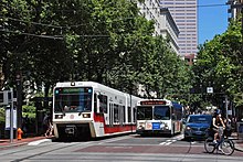 Фотография поезда Max слева, автобуса в центре и женщины на велосипеде, сворачивающей с Portland Transit Mall.