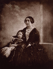 Photograph of a seated young matron (Victoria) cuddling a child next to her
