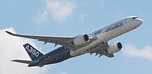 Farbfotografie in der Untersicht von einem Flugzeug in der Luft. Auf dem blau-weißen Flugzeug steht „A350 Airbus“.