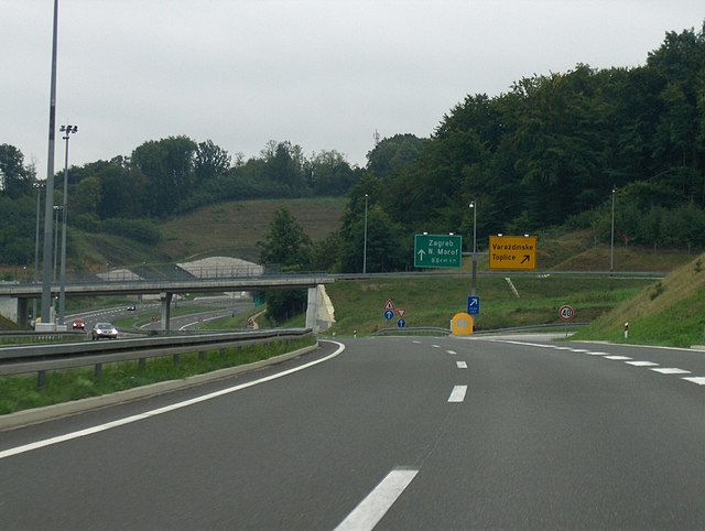 Motorway approaching a typical exit and a flyover, directional signs placed on a cantilevered gantry are visible to a side of the road