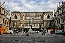 Photographie en couleurs du bâtiment principal de face, depuis l'autre côté de la place, que l'on voit occupée par des installations artistiques.