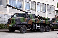 Un camion militaire surplombé d'un canon, stationnant devant un bâtiment.