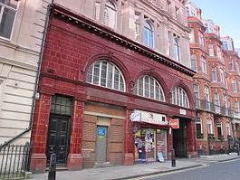 Station building faced in red glazed blocks with three large semi-circular windows at first floor level. Part of the ground floor is occupied by a shop and part has been bricked-up with a small service door