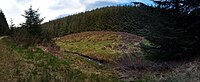 >A side view panoramic photograph of the Wormy Hillock burial mound, showing the small river which runs next to it.