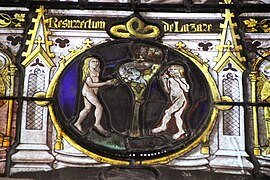 Médaillon de vitrail médiéval représentant la Tentation d'Adam et Eve, un homme et une femme sont nus autour d'un arbre portant des fruits et dans lequel il y a un serpent, la femme tient une pomme et l'homme a commencé à en manger une autre
