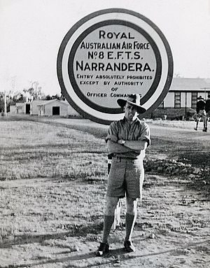 Informal portrait of uniformed man in slouch hat standing in front of sign reading "Royal Australian Air Force No. EFTS Narrandera"